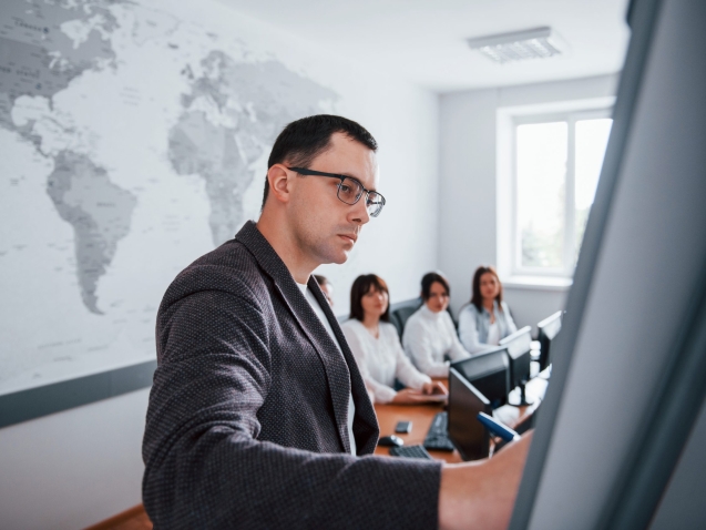 Showing example on the whiteboard. Group of people at business conference in modern classroom at daytime.